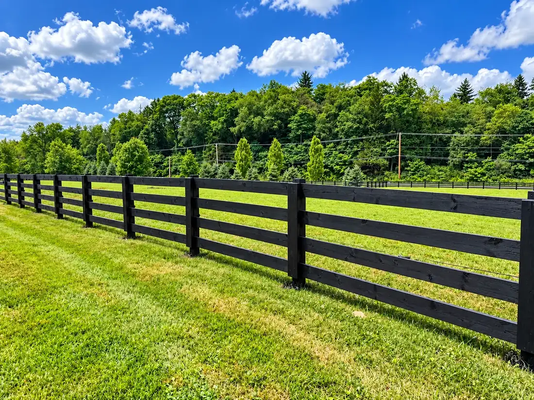 Black four-board fence running along a mowed pasture